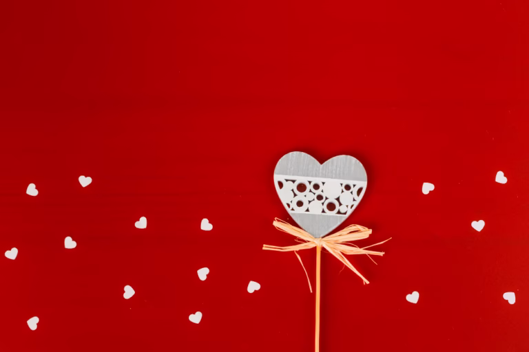 Valentin-napi ajándék ötletek. A fotón piros háttér előtt egy szív látszik, ami világosz pasztell színű papírból van kivágva.