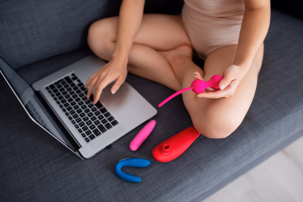 Akkus vagy elemes vibrátor közötti választást illusztrálja a fotó. Egy nő fehérneműben, különböző intim játékokkal körülvéve keresgél egy laptopn