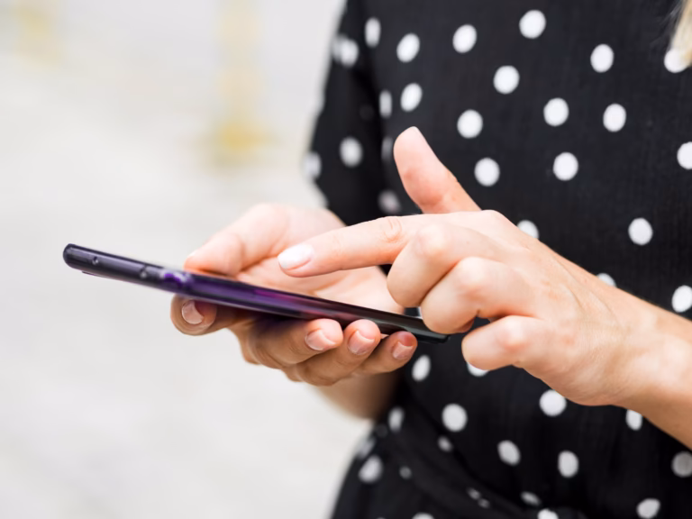 a fotón egy női kéz látható, amint éppen egy mobil telefonon navigál. A fotó illusztráció a távirányítós vibrátorokról szóló blog bejegyzéshez.